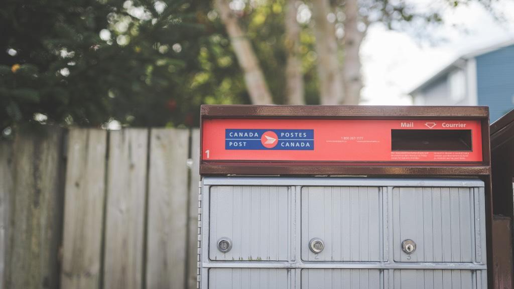 a Canada Post mail box sits in front of a wooden fence